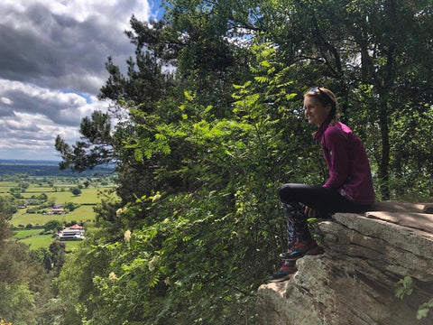 woman hiker sitting on rock looking at view with trees and sky behind
