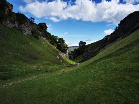 Peak District view of valley and green hillsides with trees and blue sky