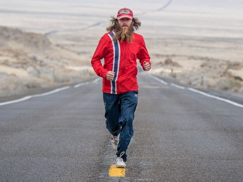 Rob Pope - man with long hair and beard wearing cap and red top running towards camera like Forrest Gump along road