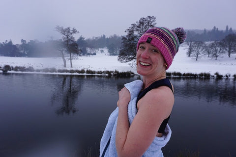 woman cold water swimming with bobble hat and snowy lake beyond