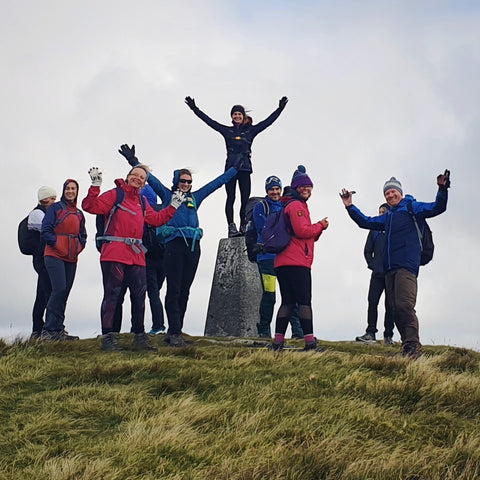 hikers on mental health walk Wales - group celebrating summit with one person standing on top of trig point