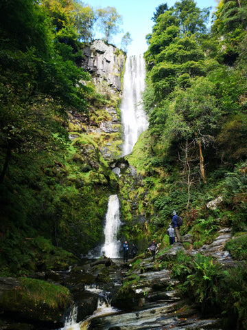 waterfall in Wales with green trees and group of hikers on mental health walk