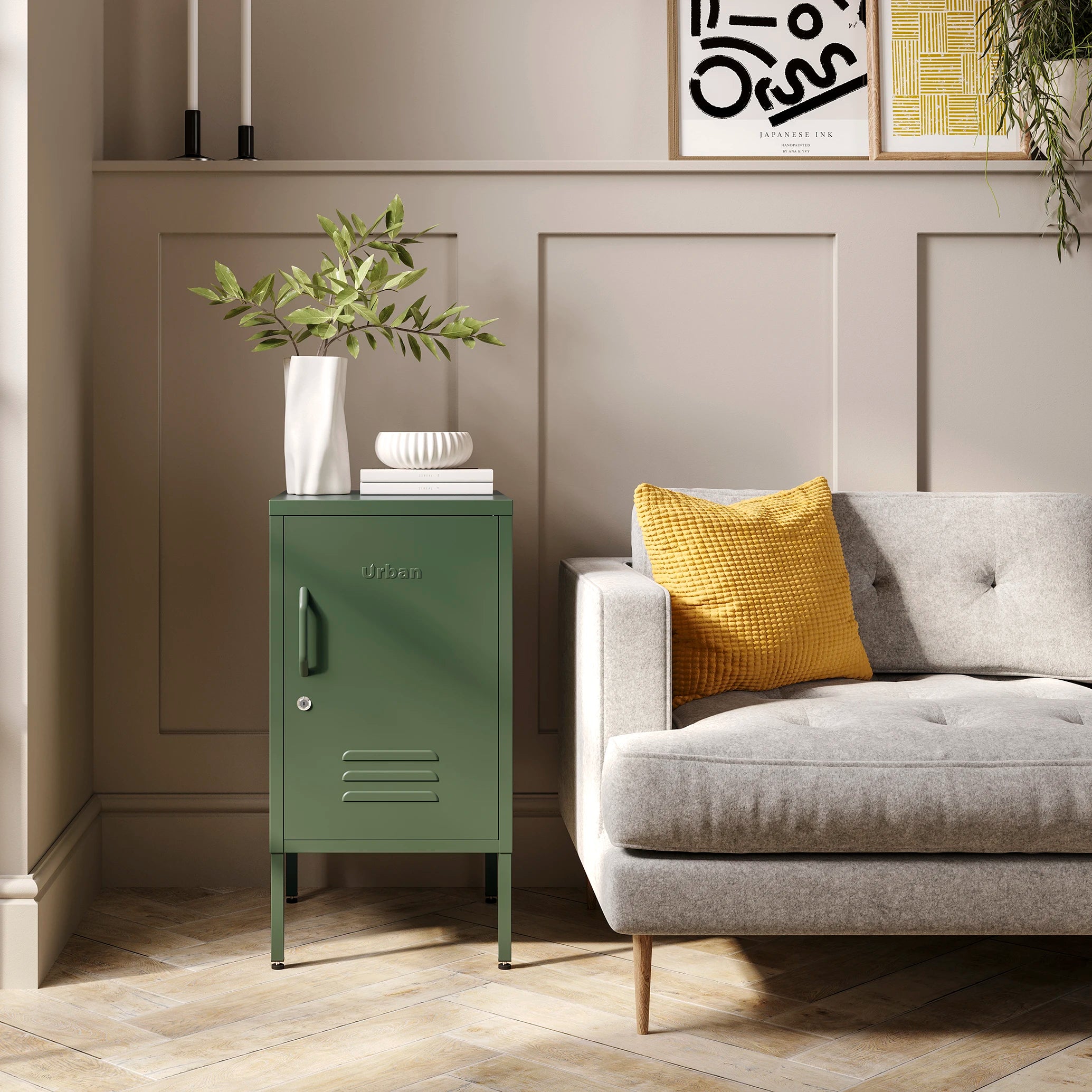 The Camden short, 1 door metal side table locker in Forest Green, beside a sofa.