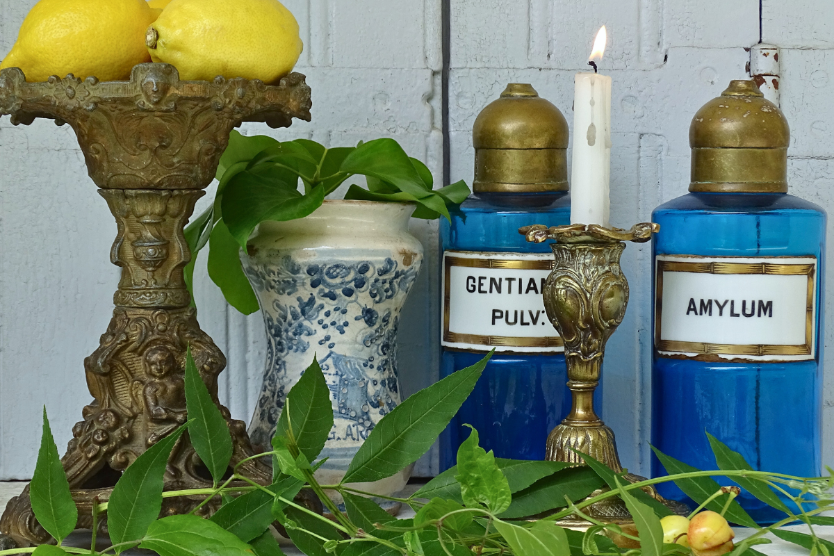 Antique French apothecary bottles with blue glass, brass tops and porcelain labels. Next to an antique Italian albarello medicine jar and two antique candle holders.