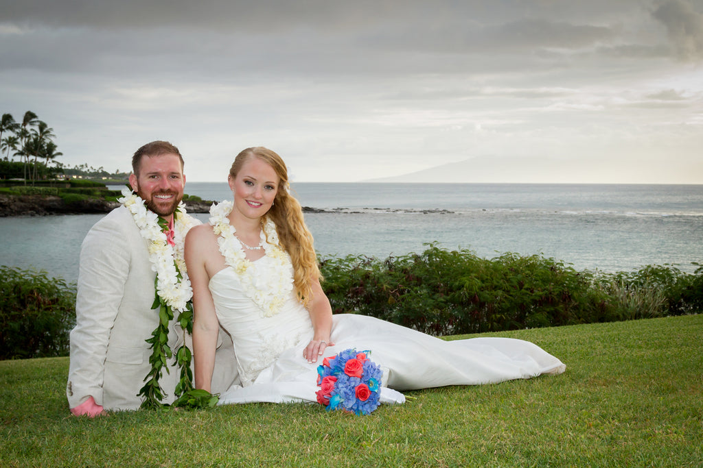 A Bride and Groom sit on a grassed area over looking the ocean