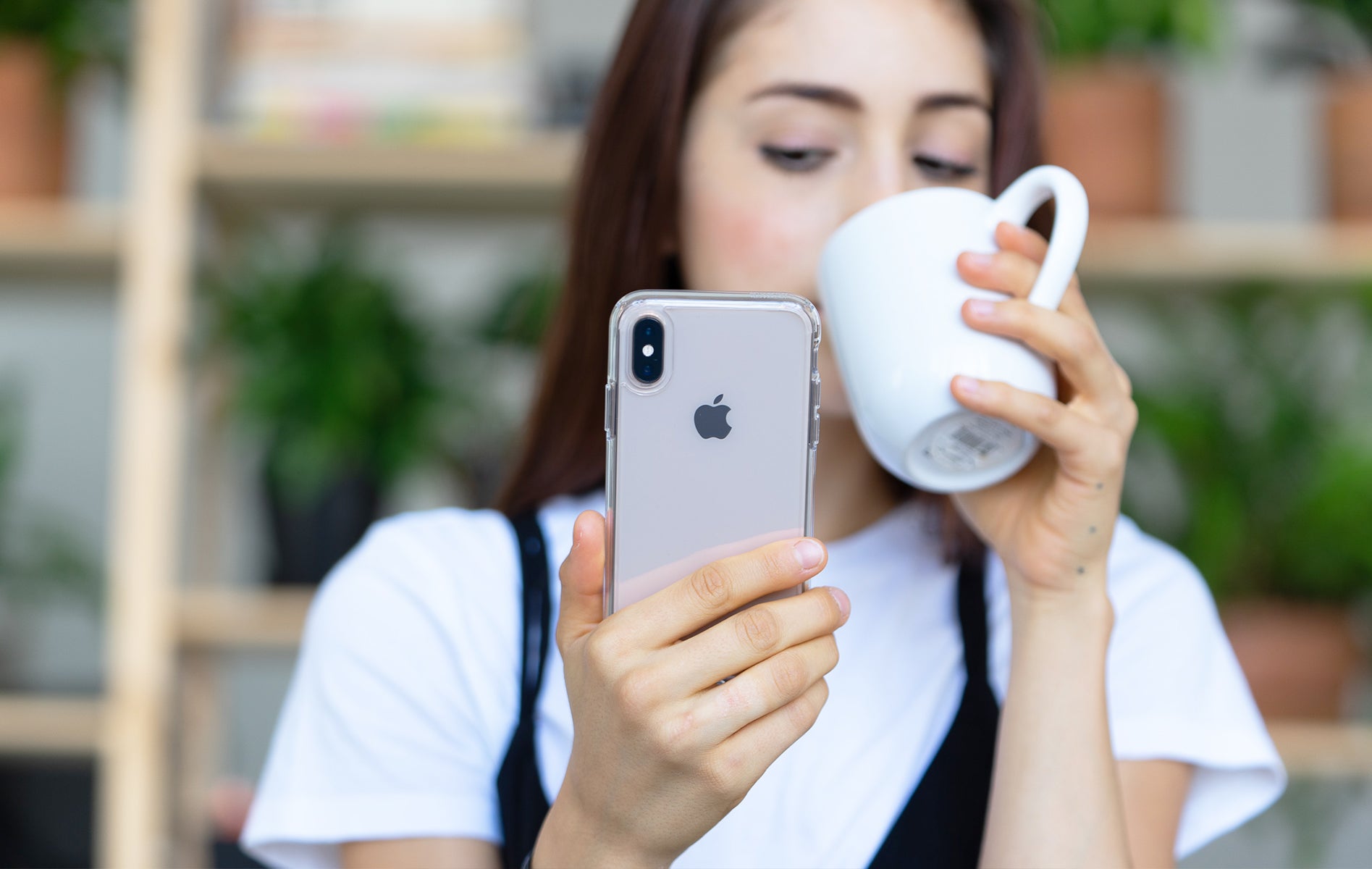 Woman holding a cup on one hand and an iPhone X with a clear case on the other.