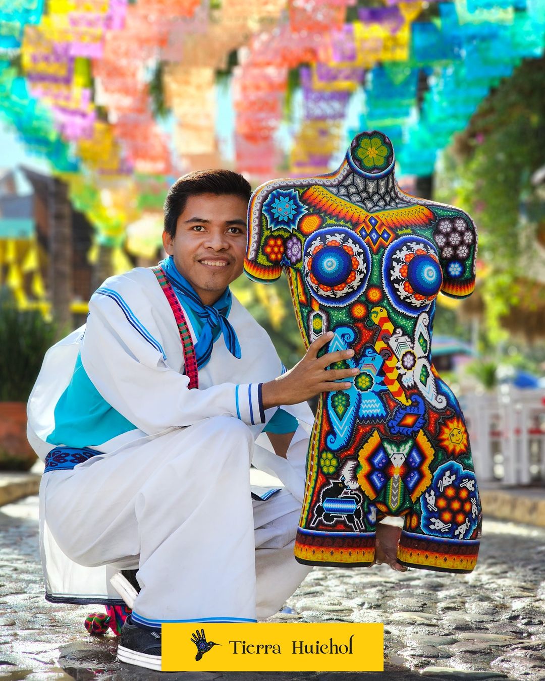 Artista Huichol con una obra de arte en sus manos que representa a un cuerpo humano intervenidos con chaquiras de colores