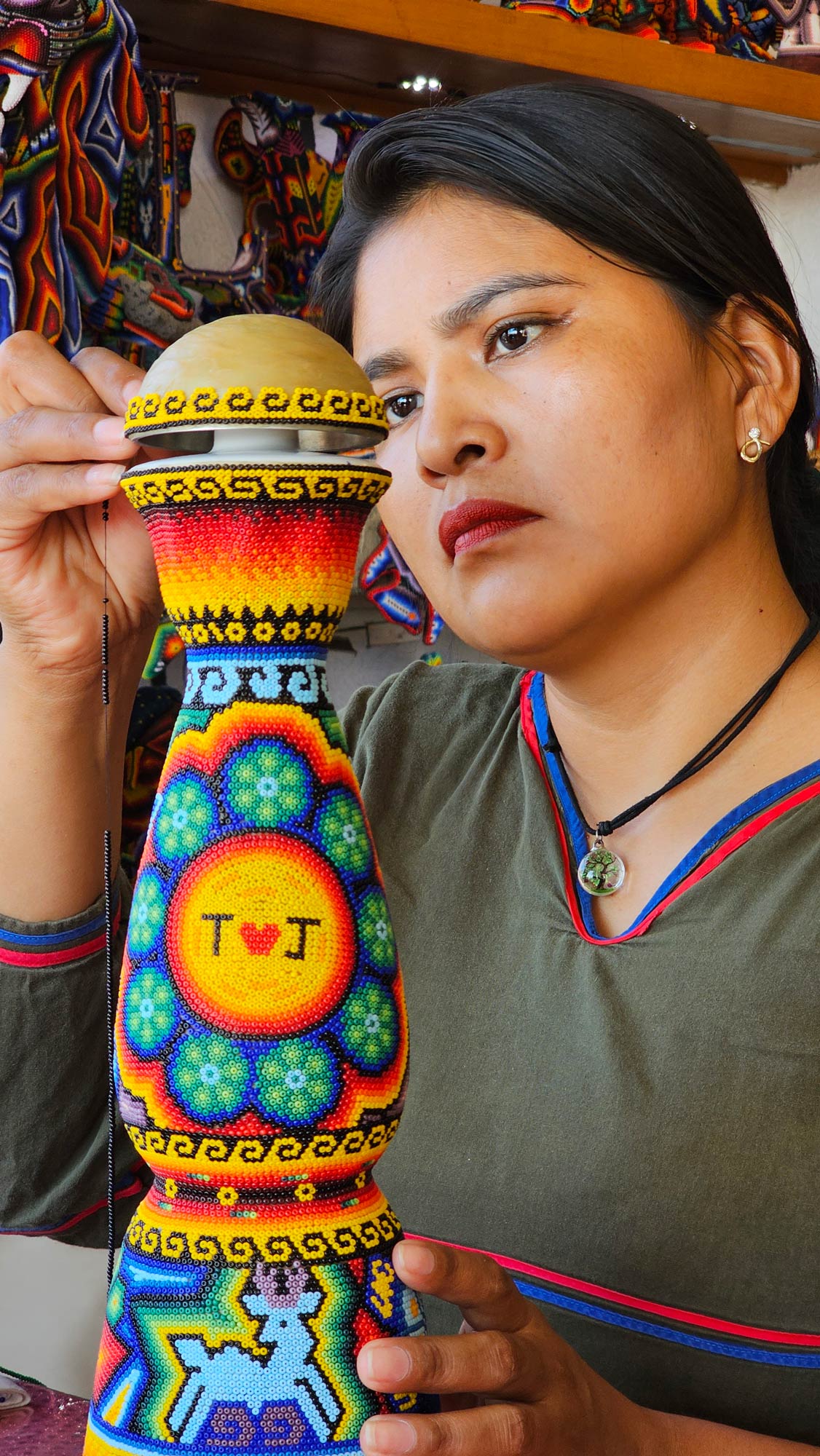 Mujer artesana huichol creando una artesania en un molde de botella de tequila co colores vividos y simbolos wixarikas