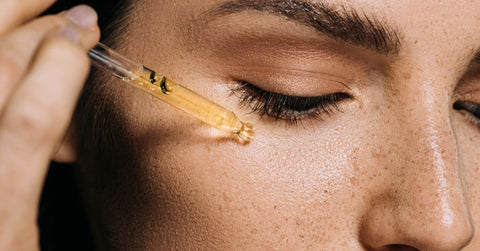 Une belle jeune femme à la peau parfaite s'applique sur la peau de l'huile végétale à l'aide d'une pipette compte-goutte en verre.