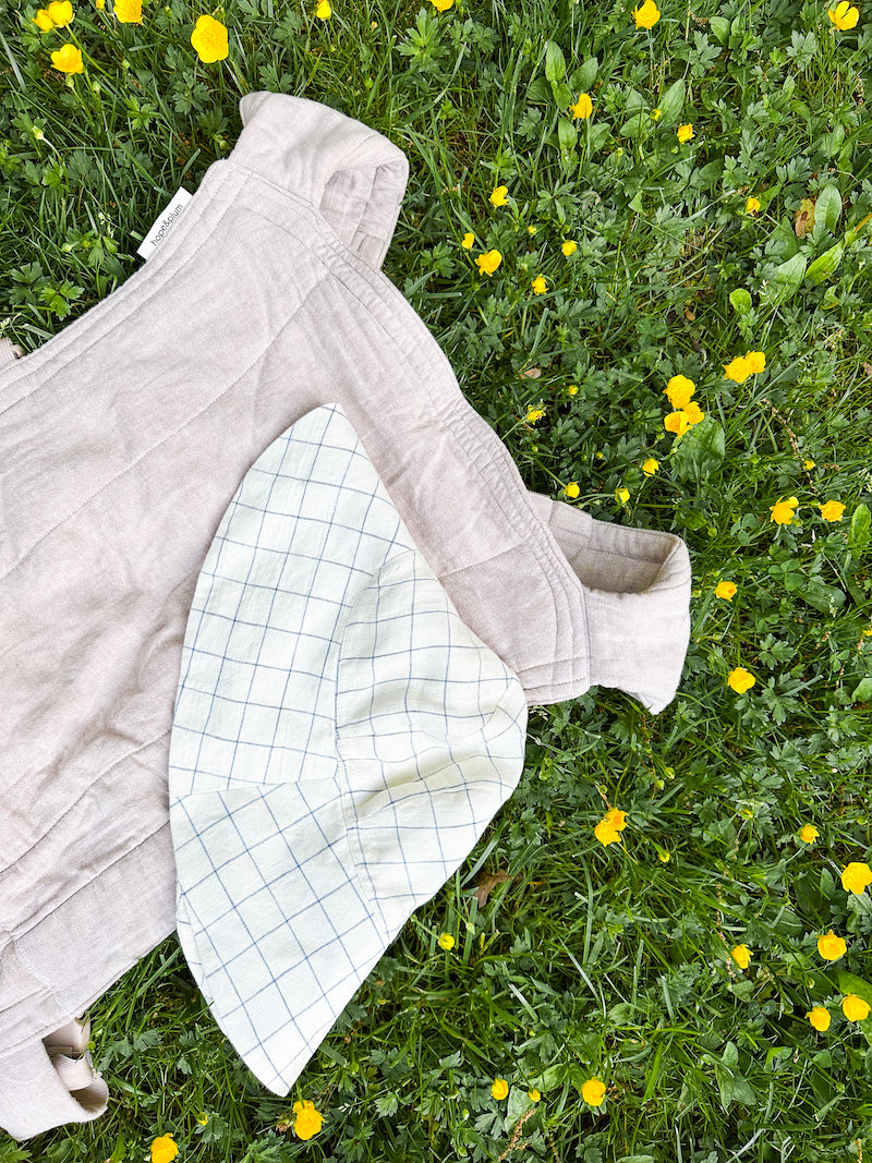 flay lay of Hope & Plum Lark baby carrier laying in the grass with a Briar Baby sunbonnet