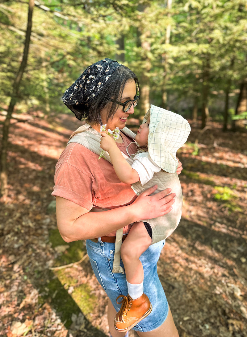 Mom on a hiking trail wearing her baby in a Hope & Plum soft-structured baby carrier.