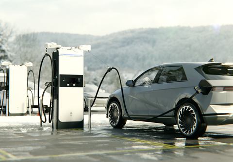 Elektrofahrzeug an Ladegerät auf verschneitem Parkplatz angeschlossen.
