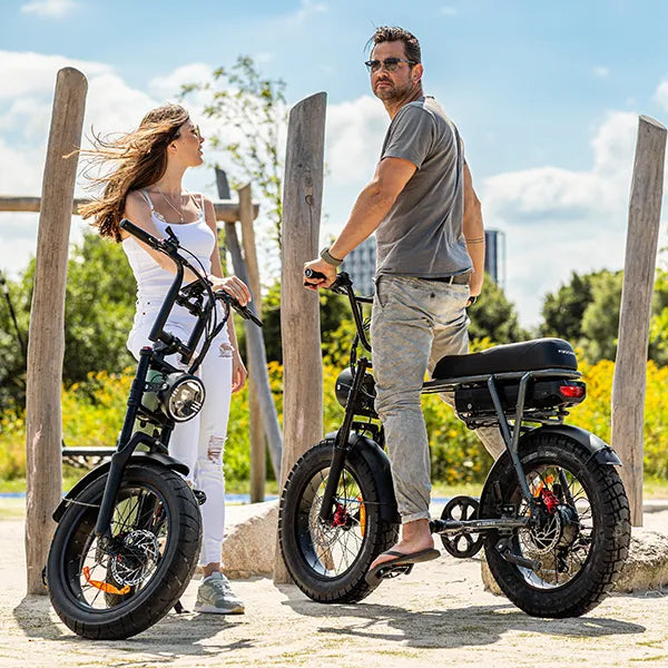 Young woman and man posing outside in the sun with two electric fatbikes