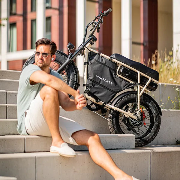 Young man sitting on concrete steps in the sun next to an electric fatbike