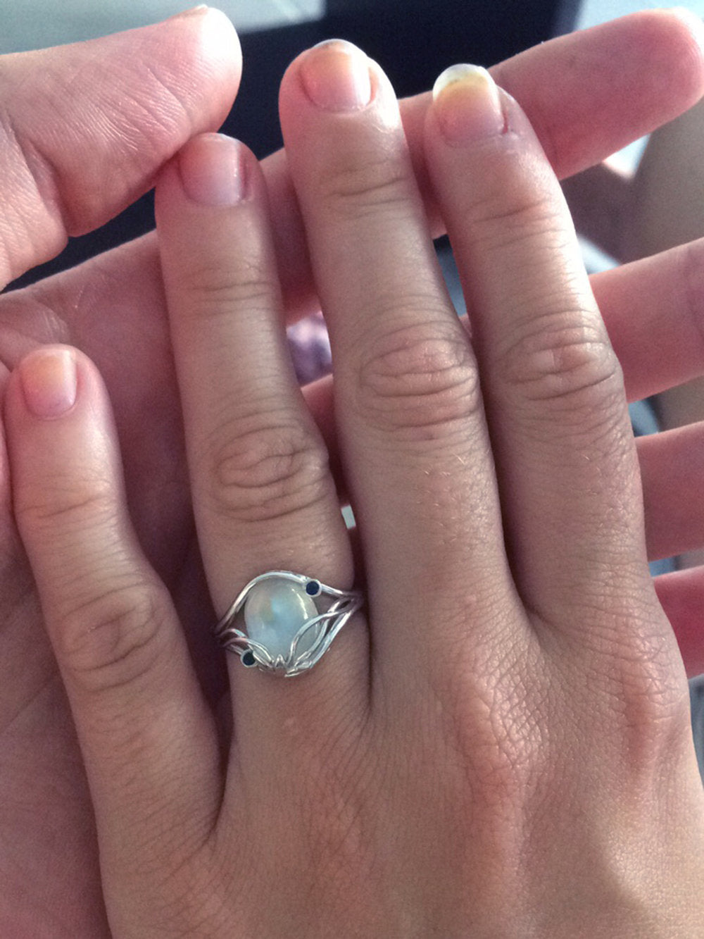 Alice's hand held by Michael's, showing off her new Elvish Moonstone engagement ring by Takayas