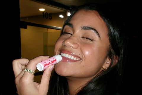 Cracked lips solution demonstrated by a smiling woman using pink "Space Camp" lip balm at night.