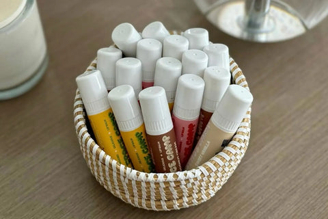 Vegan lip balm collection in assorted flavors arranged neatly in a woven basket on a wooden surface.