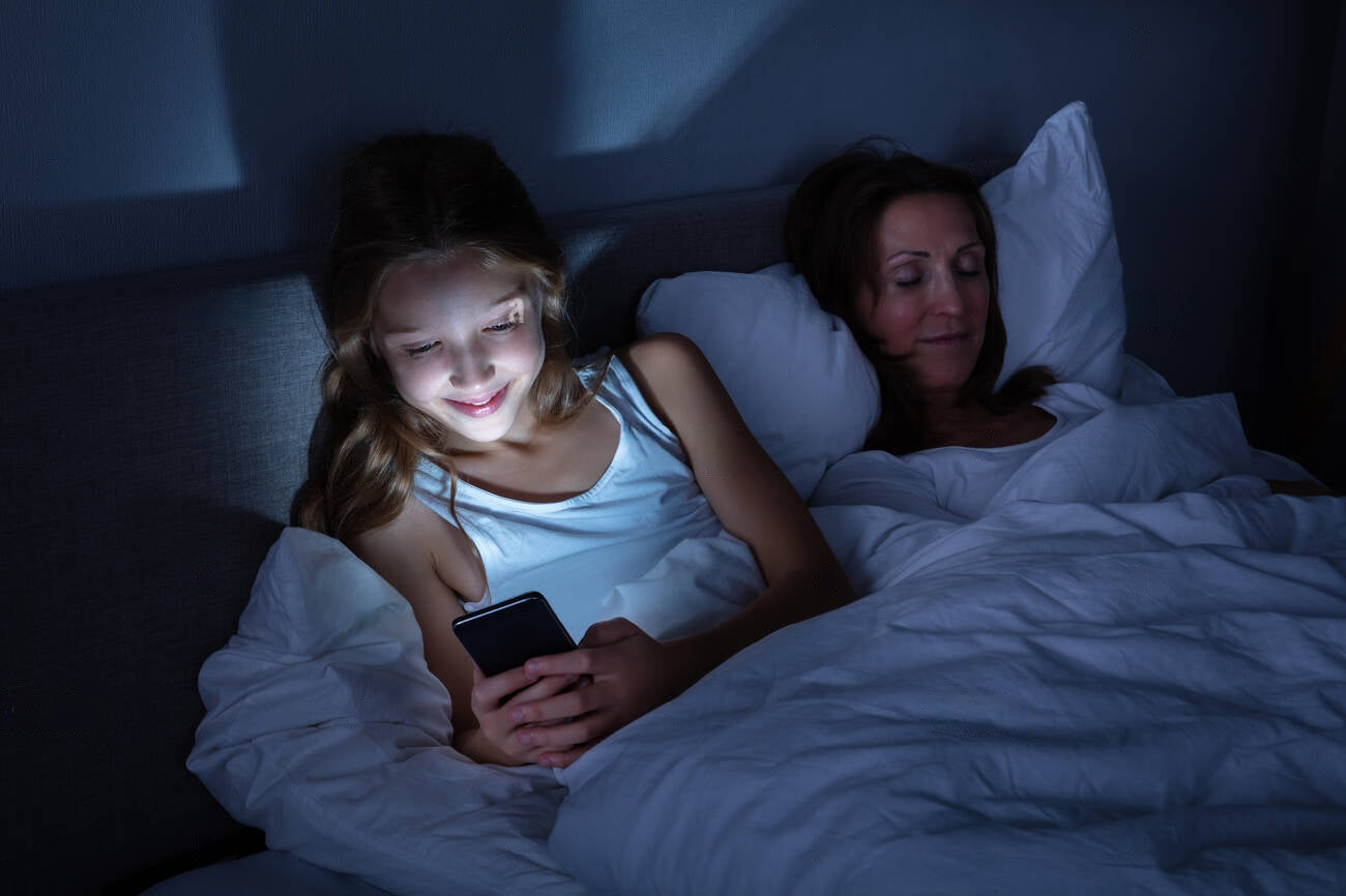 happy-girl-using-mobile-phone-while-her-daughter-sleeping-on-cozy-bed-at-night-R7A7RX-transformed copia.jpg__PID:36dc0d4f-7488-4fa8-b772-ec597e3c0514
