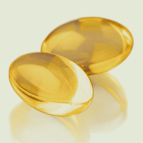 Two yellow, transparent, oval-shaped Vitamin E gel pills displayed against a neutral background.