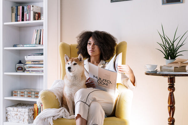 A woman with curly hair sitting on a yellow chair with her dog