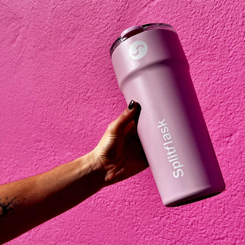 Woman’s outstretched hand holding a Splitflask hot and cold tumbler With a pink background
