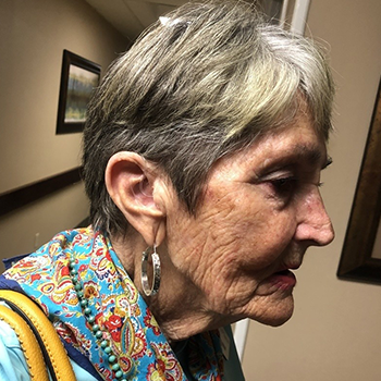 Profile view of an elderly woman wearing a colorful scarf and hoop earrings.