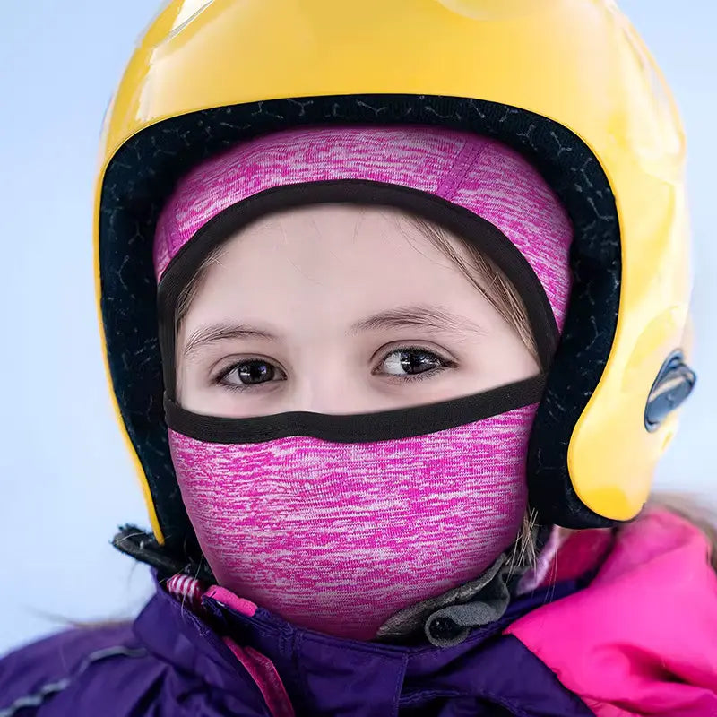Child wearing a pink thin balaclava under a yellow helmet, ready for a winter outdoor activity.