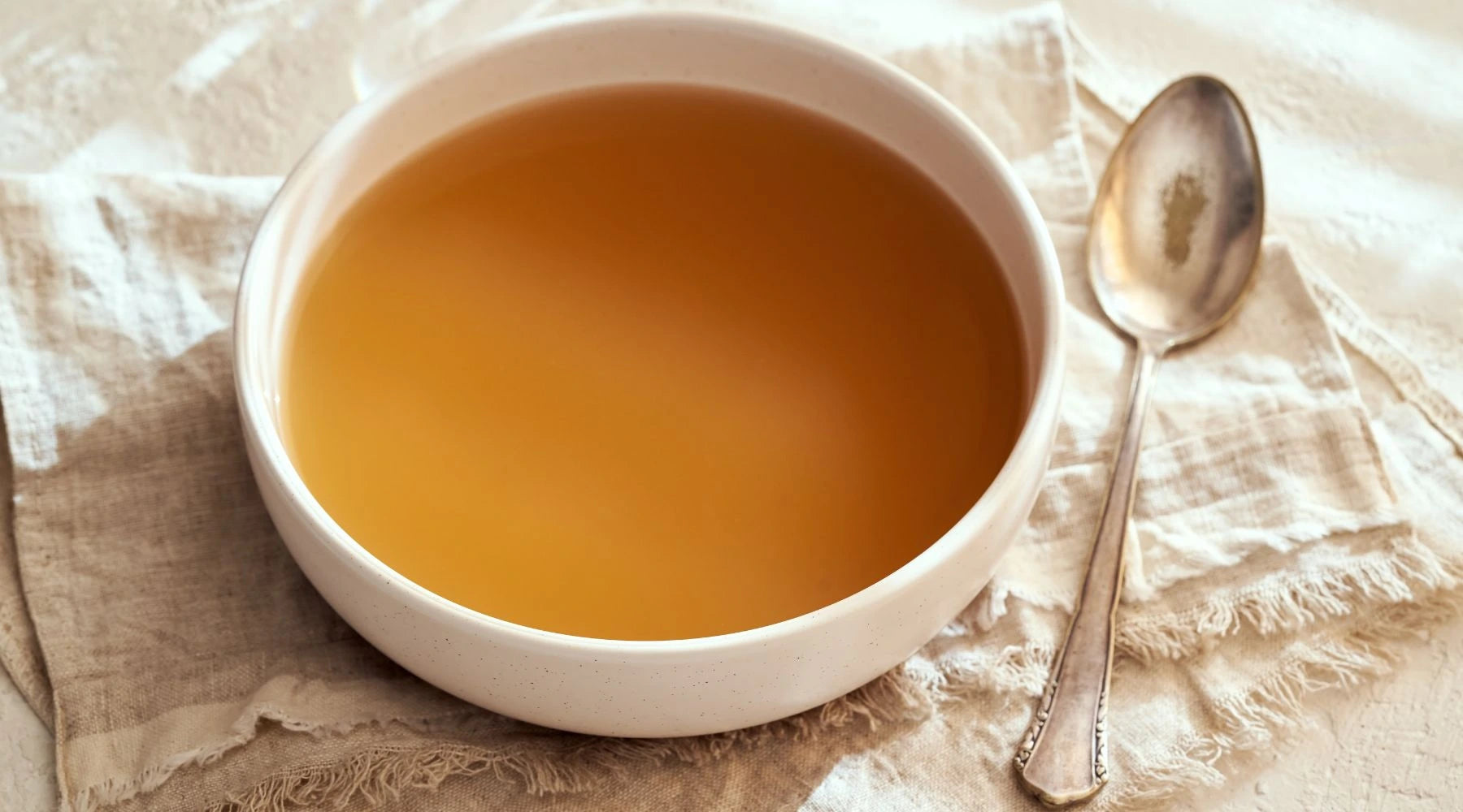 Warm bowl of homemade bone broth on natural linen – slow-simmered for gut healing, joint support, and whole-body nourishment