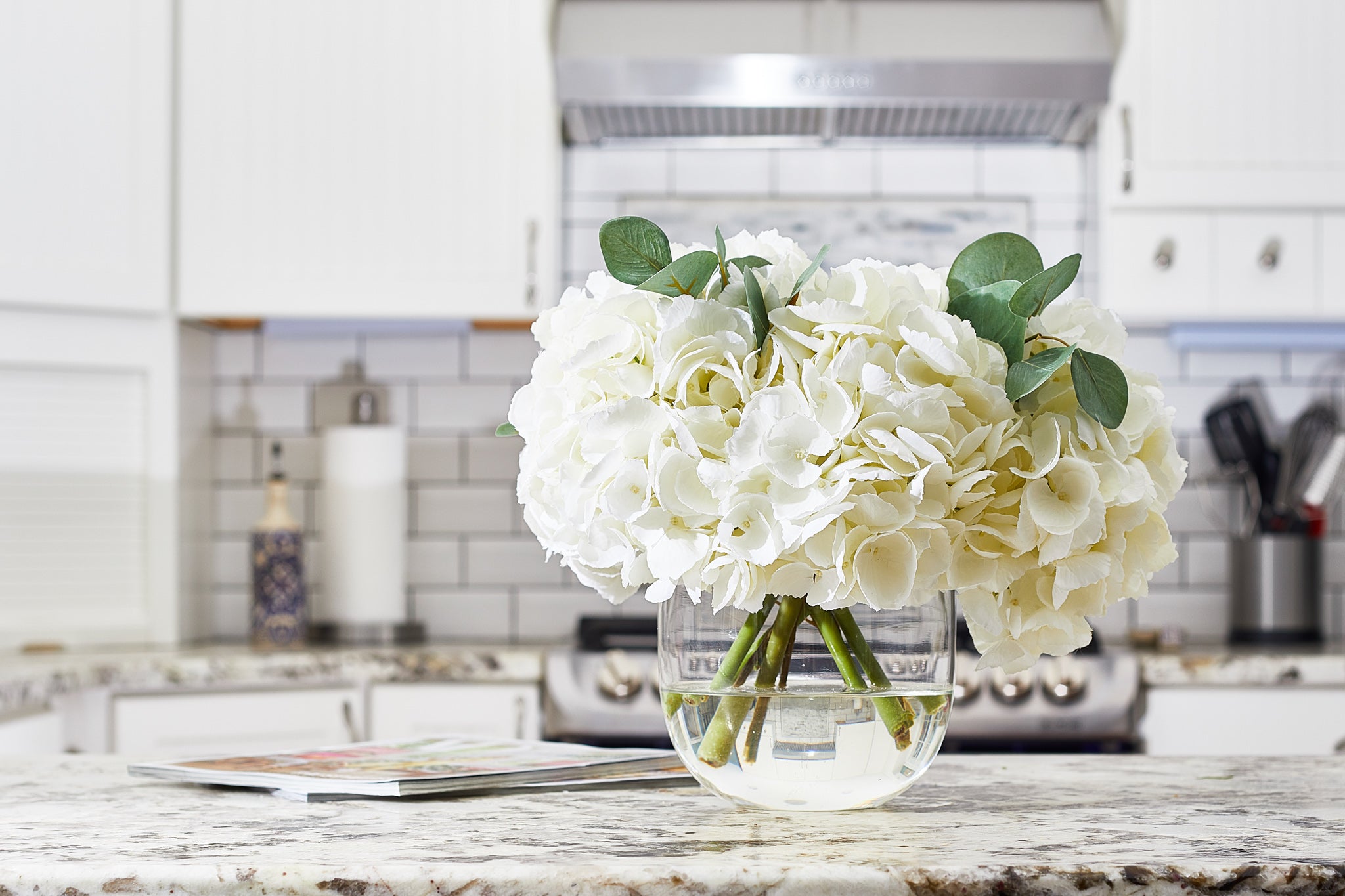 Large White Hydrangea And Eucalyptus Arrangement In Rounded Glass Vase