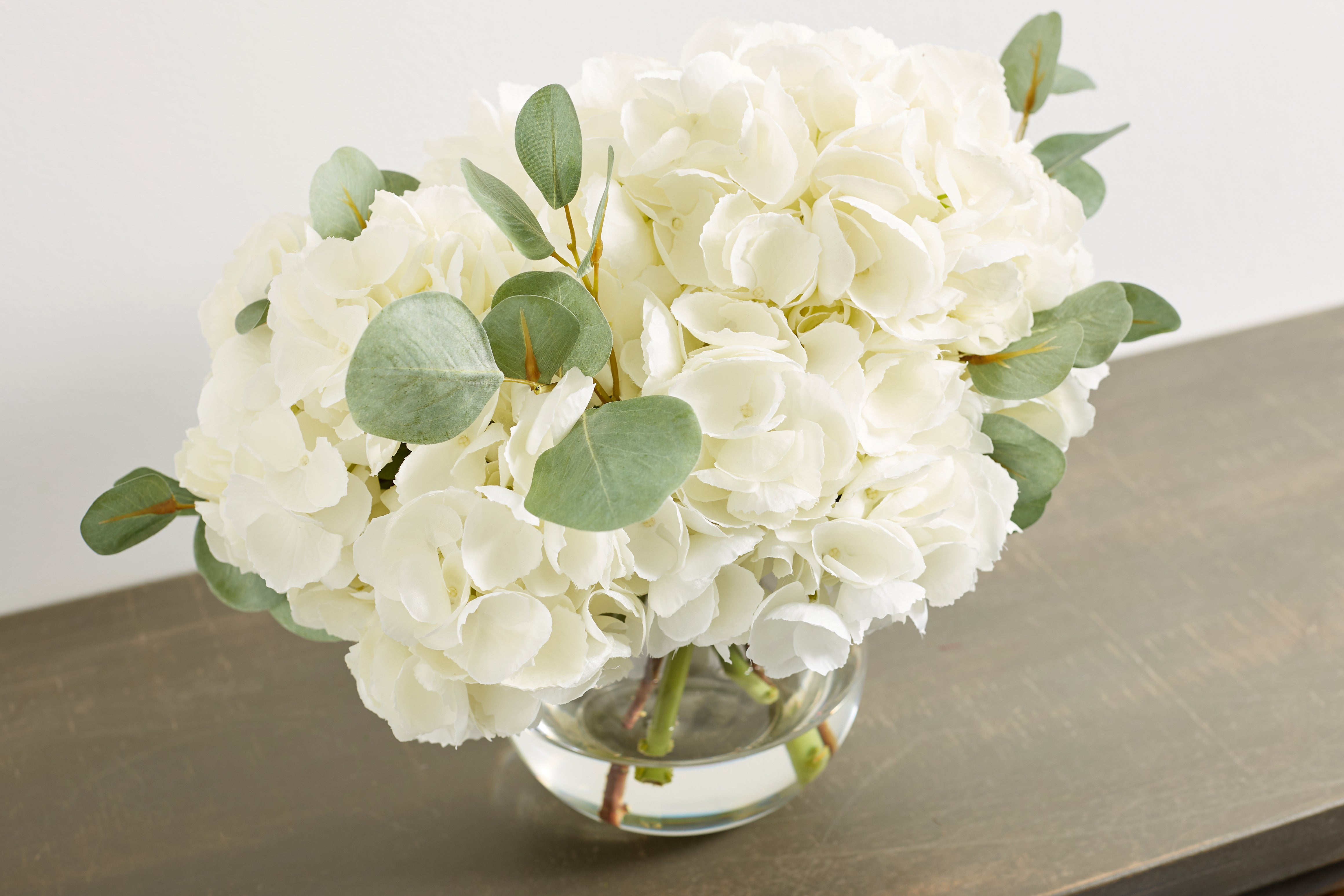 Large White Hydrangea And Eucalyptus Arrangement In Rounded Glass Vase