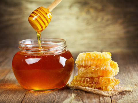 A jar of honey being used as a cocktail substitute for simple syrup. There is a honeycomb on the table next to it.