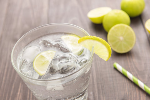 Vodka Press cocktail with lime wedges and a straw, on a wooden table