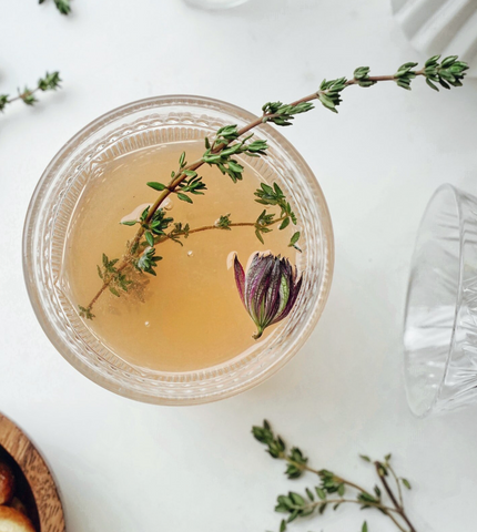 a sprig of olive green thyme rests in a glass cup of tea