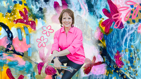 woman artist seated with brushes in hand in front of colored background