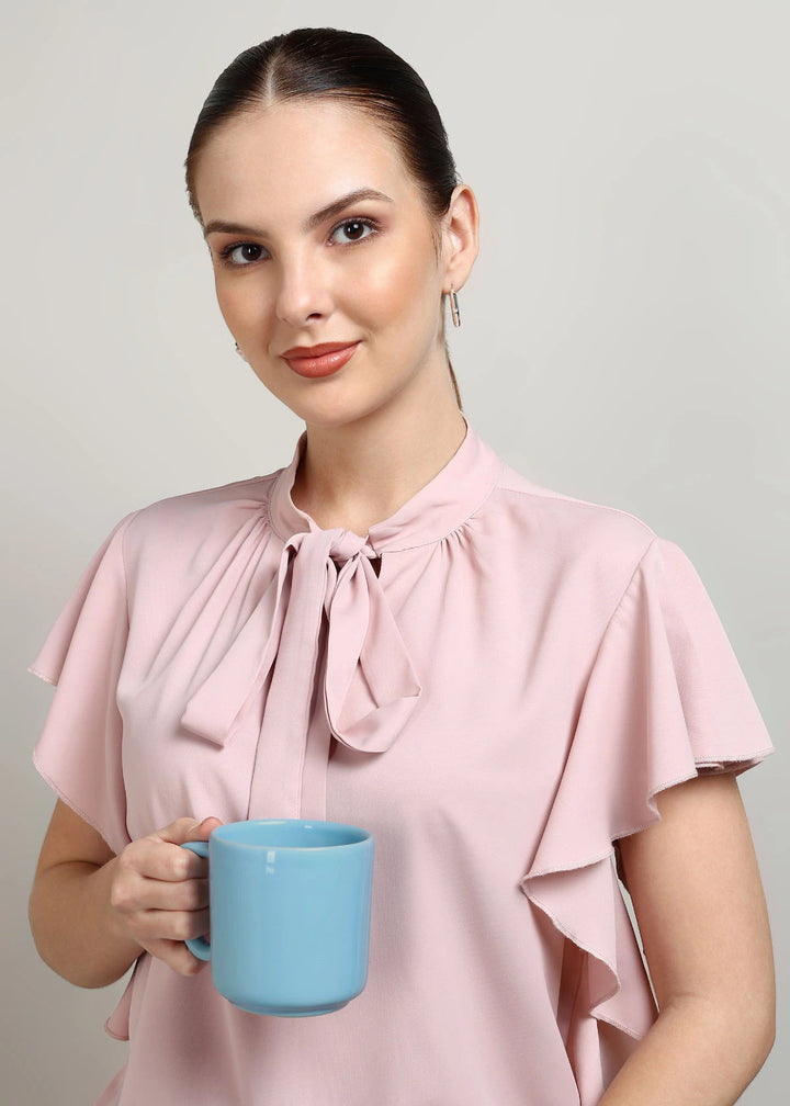 Woman in a pink blouse holding a blue mug against a plain background