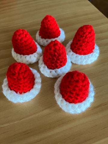 6 small crochet santa hats, in red and white, sitting on a table