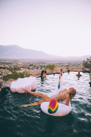 Kololo Big Unicorn girl in gold swimsuit lounging with Pink Seashell floaty in the background