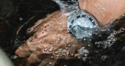 Man dipping his hand on water while wearing a watch