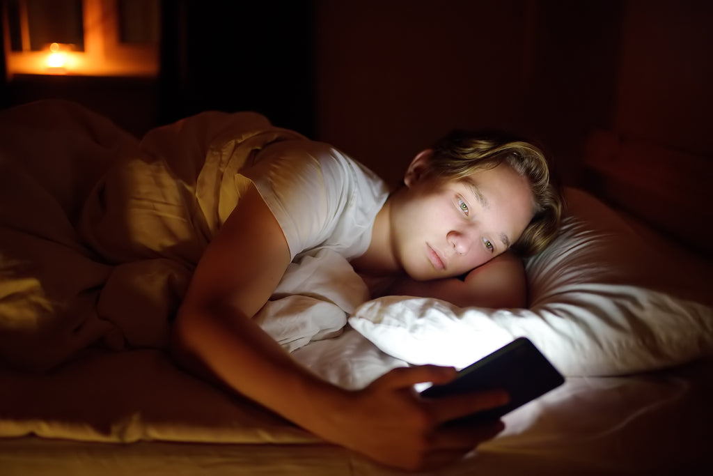 Gutt i tenårene som scroller på mobilen i sengen og forstyrrer søvnen sin