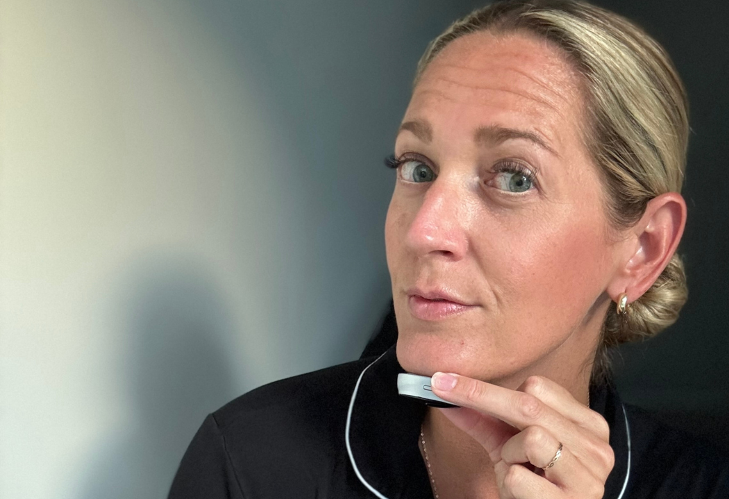 Woman holding a small device under her chin in a well-lit room.