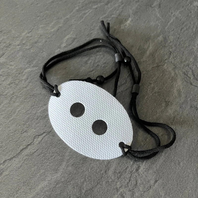 A white oval tag with two holes and black strap laces on a grey surface.