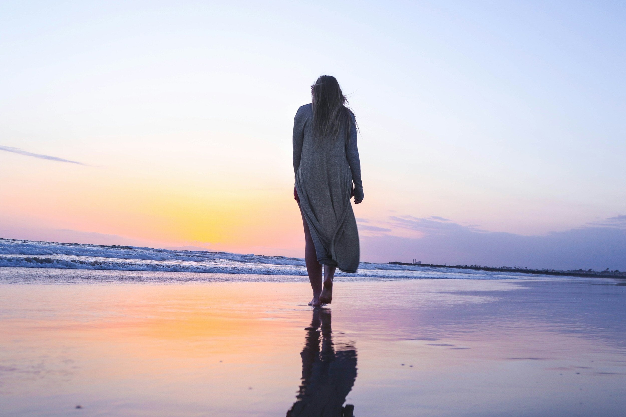 tranquil beach scene with the reflection of the sunset on the sand and a woman peacefully walking in the serene landscape