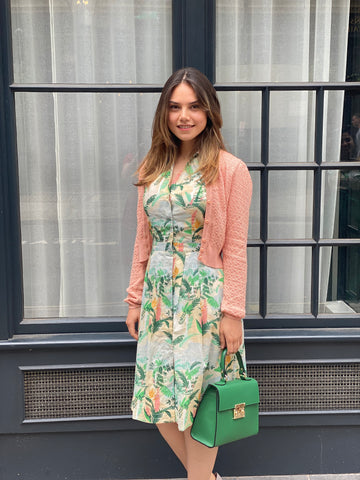 Model in floral print shirt dress and pink cardigan holding green vintage style handbag