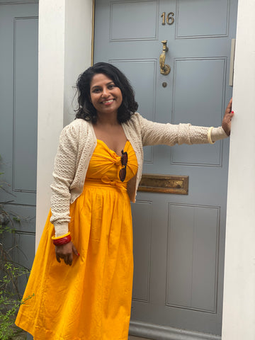 Model leaning on doorframe wearing yellow Salma sundress and linen coloured Delightful Daytime Cardigan with bangles and sunglasses