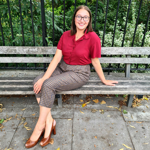 Vintage inspired cropped trousers worn with burgundy blouse by Alex who sits side on, on a wooden bench smiling