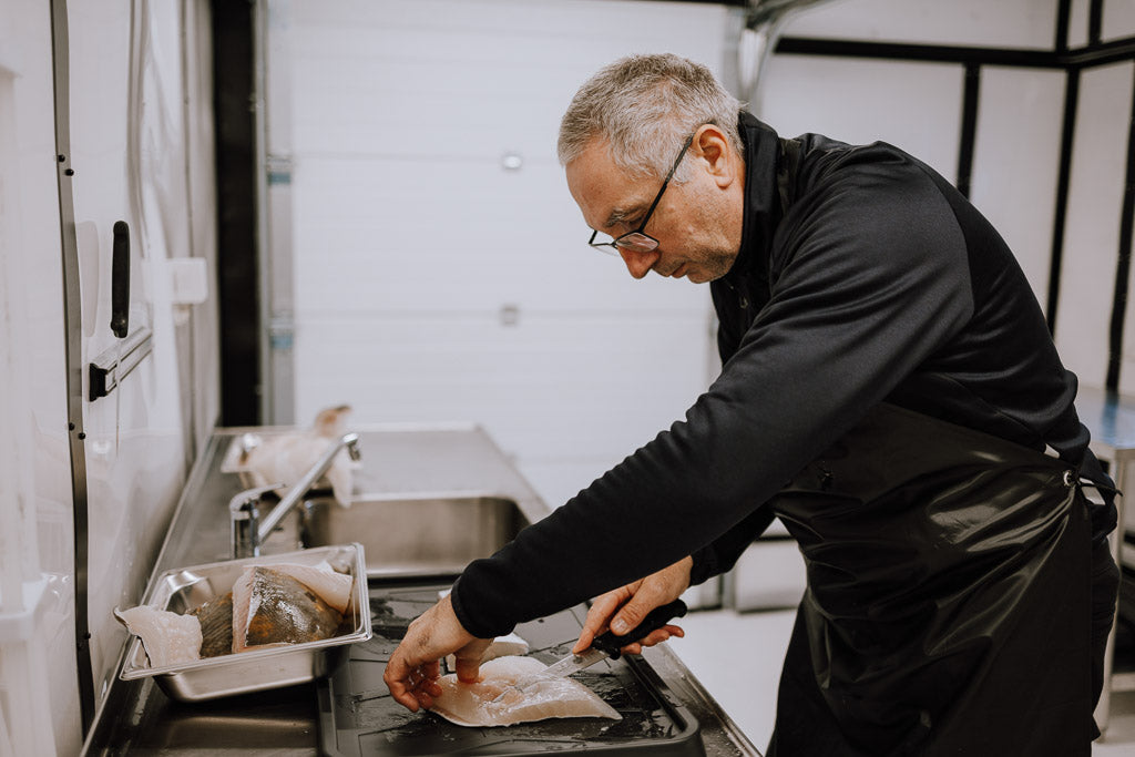Kjell Ivar som skjærer fisk i produksjonslokalet til Storvik Gård. Foto.