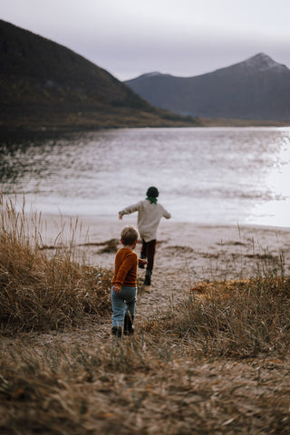 Barn i ullklær som løper på en strand. Foto.