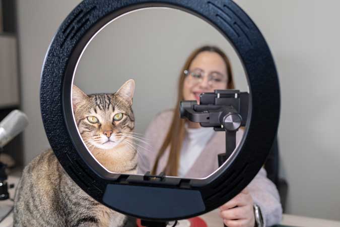a lady and a cat taking a picture in front of a ring light device
