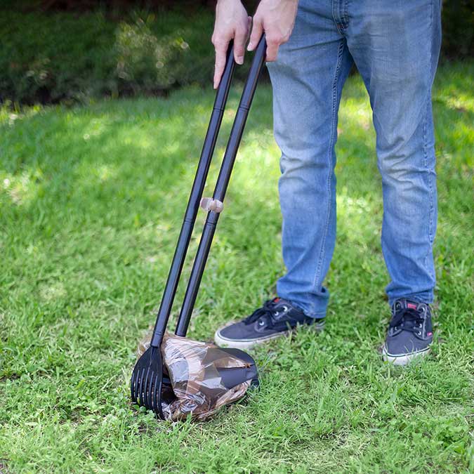 a man using a dog poop scoop bin and rake to pick up dog poop from grass