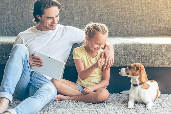 a man and a little girl sitting on the floor with their dog smiling at their dog